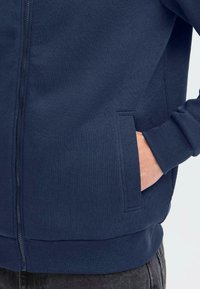 Jūrinio stiliaus zip-up kapučino džemperis, pagamintas iš minkštos medvilnės mišinio. Turintis šonines kišenes, prigludusias rankoves ir lygią tekstūrą, tinkantis kasdieniam dėvėjimui.
