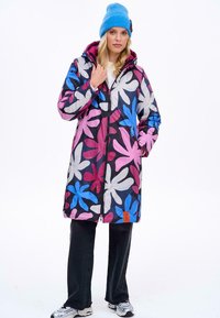 Barevný, vzorovaný kabát s černým, růžovým, modrým a bílým květinovým vzorem. Obsahuje přední zip, kapuci a polodlouhý střih. Materiál vypadá texturovaně.