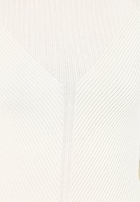 Weißes, geripptes Strickoberteil mit einem V-Ausschnitt, texturierten Linien und einer engen Passform, die die weichen, flexiblen Eigenschaften des Materials betont.