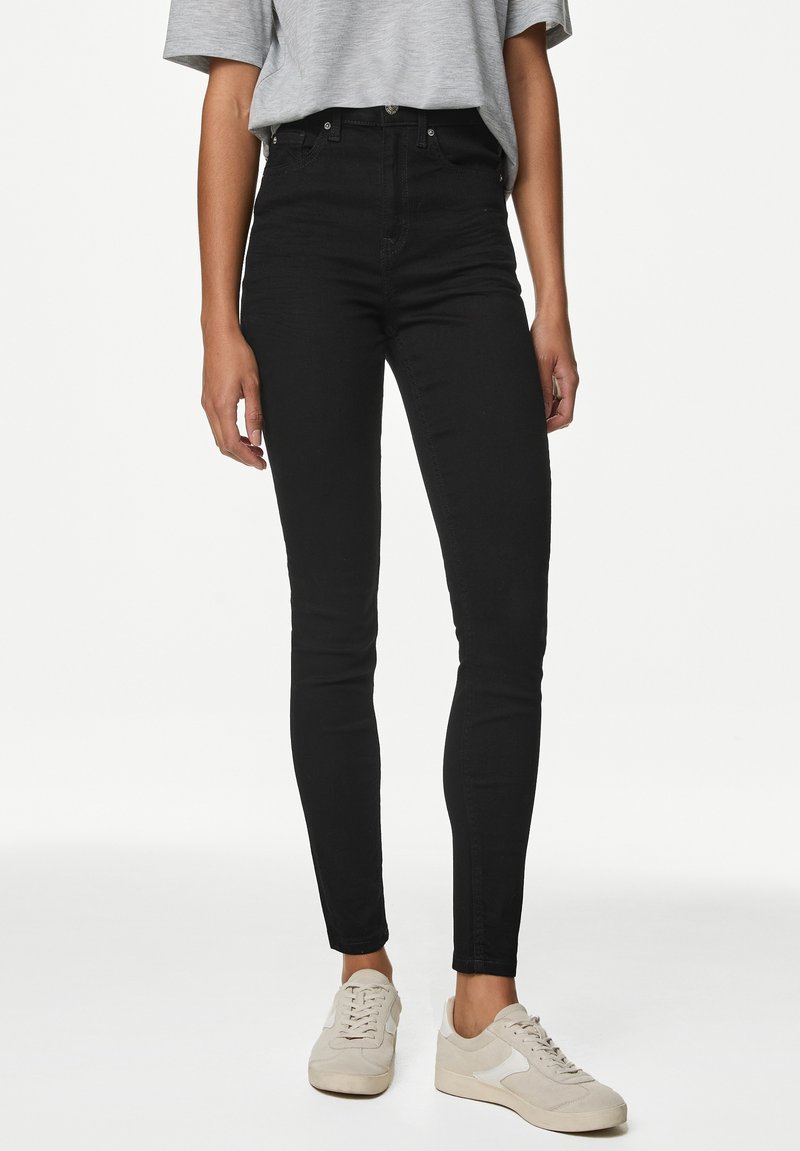 Högmidjade svarta jeans med smal passform, tillverkade av denim. I kombination med en grå t-shirt och beige sneakers, med klassisk knappstängning.