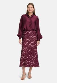 Burgundy satin blouse with a relaxed fit and button closure, paired with a burgundy polka dot skirt. Clear strappy heels complete the look.