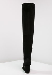 Botas negras por encima de la rodilla hechas de suave ante, con un tacón bloque, cierre con cremallera lateral y una textura suave.