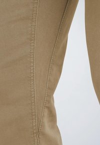 Pantaloni beige, aderenti, realizzati in tessuto misto cotone. Presentano cuciture laterali evidenti e una superficie liscia. Nessun motivo visibile o elementi metallici.