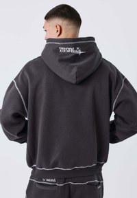 Sudadera con capucha gris con detalles de costura blanca, con una gran capucha y un logo en la parte posterior. Hecha de una tela suave, de corte relajado.