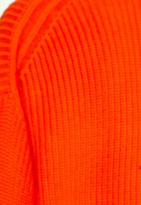 Gros plan sur un tissu tricoté orange vif montrant des motifs de couture côtelés et texturés.