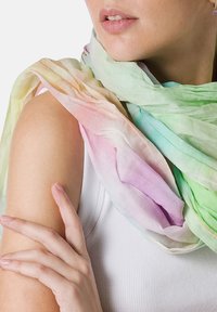 Scarf leggero e multicolore in tonalità pastello di verde, rosa e viola. Texture morbida con un design arioso, drappeggiata intorno alla spalla.