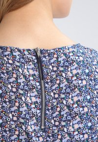 Back view of person wearing blue floral dress with visible metal zipper running down center of upper back.