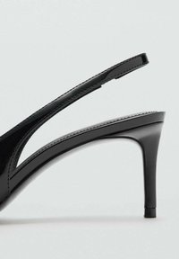 Zapato de tacón alto de charol negro con talón escarpín, punta afilada y diseño elegante y minimalista. Cuenta con una tira fina y un tacón estable.