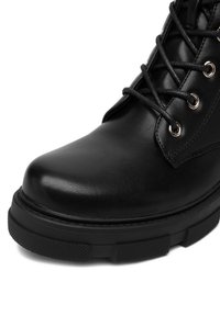 Čierne kožené členkové čižmy s okrúhlou špičkou, so šnurovaním, kovovými očkami a textúrovanou gumovou podrážkou. Majú hladký povrch a robustnú konštrukciu.