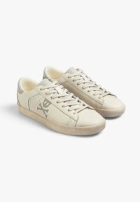 Sneaker beige realizzate in pelle liscia, con un discreto logo di teschio e ossa incrociate, punta rotonda e suola sagomata di colore chiaro.