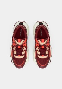 Red and beige mesh sneakers with thick white soles, featuring contrasting accents and textured panels. Laces integrated with a pull tab.