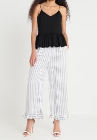 Top peplum negro con tirantes finos, combinado con pantalones de pierna ancha a rayas blancas que tienen dobladillos con volantes. La modelo lleva tacones blancos de tiras.