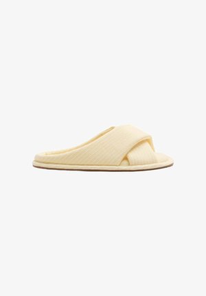 Cremefarbener Slip-On-Hausschuh mit gesteppte, überkreuzten Stoffriemen und flacher Sohle vor weißem Hintergrund.
