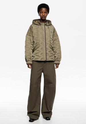 Chaqueta acolchada verde oliva con capucha, que cuenta con un cierre frontal, bolsillos laterales y puños elásticos, combinada con pantalones anchos en color oliva.