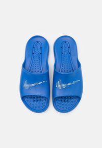 Blue slide sandals with a smooth plastic upper and textured footbed, featuring a white dotted Nike logo on the outer strap.