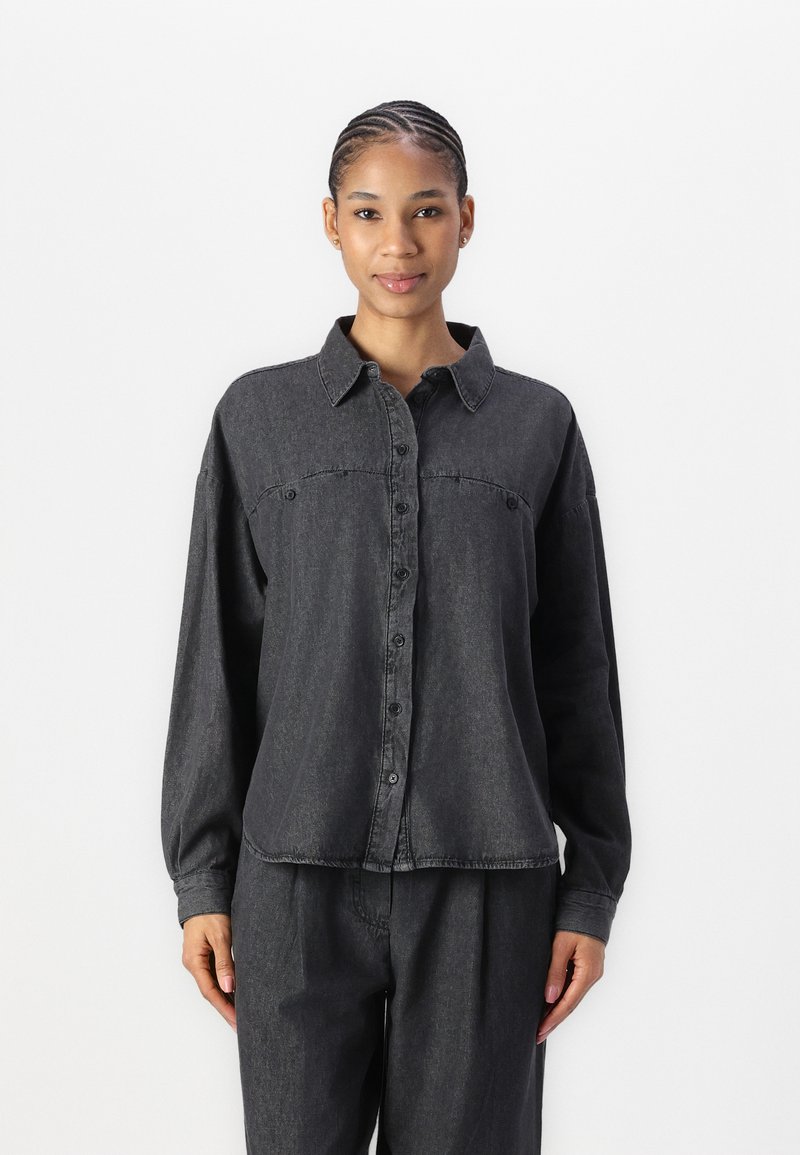 Camisa de botão em denim cinza escuro com colarinho, bolso único no peito e mangas longas. O tecido é ligeiramente texturizado e tem um corte descontraído.