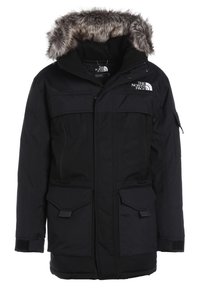 Parka d'hiver isolée noire avec capuche bordée de fourrure, multiples poches avant, et logo The North Face sur la poitrine et à l'intérieur du col.