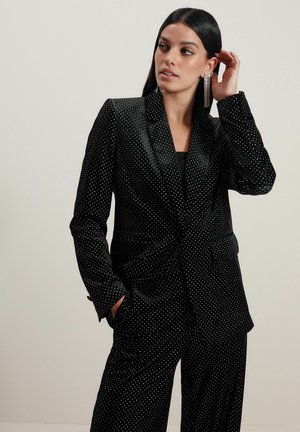 Sort polka dot jakkesæt med en tætsiddende blazer og brede bukser, lavet af glat stof; har en spidset krave og sidelommer.