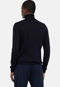 Donkerblauwe coltrui met een aansluitend ontwerp, lange mouwen en geribbelde boorden en zoom, gemaakt van een zachte, gestructureerde stof.