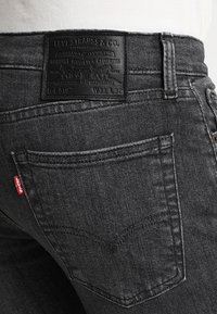 Jeans de mezclilla gris oscuro con un parche de cuero con el nombre de la marca y detalles en relieve, bolsillo trasero con etiqueta de marca roja, diseño ajustado.