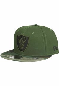 Grüne Baseballmütze mit einem schwarzen Raiders-Logo auf der Vorderseite, einem Schirm im Camouflage-Muster und einem strukturierten Design mit Nähdetails.