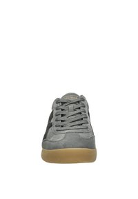 Zapatilla de ante gris con acentos negros, puntera redonda y suela de goma texturizada. Presenta cordones planos grises y un sutil logo en la lengüeta.