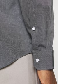 Donkergrijze overhemd met lange mouwen en een gestructureerd, dun gestreept patroon. Voorzien van knoopmanchetten met witte knopen en een licht gebogen zoom.