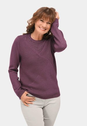 Lila gestrickter Pullover mit strukturierten geometrischen Mustern, Rundhalsausschnitt und langen Ärmeln, kombiniert mit hellen Hosen.