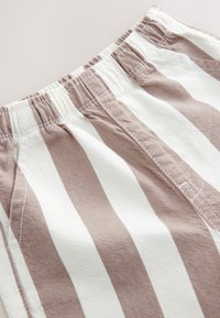 Tessuto di cotone a righe con strisce alternate color beige chiaro e marrone, dotato di una cintura elastica e dettagli di cuciture visibili.