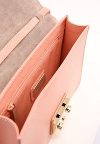 Różowa skórzana torebka z gładką zewnętrzną powierzchnią, zamszową podszewką, złotymi okuciami oraz wieloma przegródkami, w tym kieszenią na zamek.