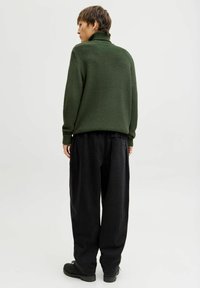 Pull-over en laine verte à col roulé avec un motif texturé, associé à un pantalon noir ample et des chaussures noires. L'ensemble présente des manches longues et des poignets.