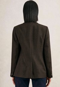 Blazer à carreaux marron et noir avec une silhouette ajustée, des épaules structurées, des manches longues et un détail d'ouverture au dos.