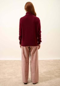 Suéter de cuello alto burdeos hecho de una tela suave, con mangas largas y puños acanalados, combinado con pantalones de pierna ancha en rosa claro.