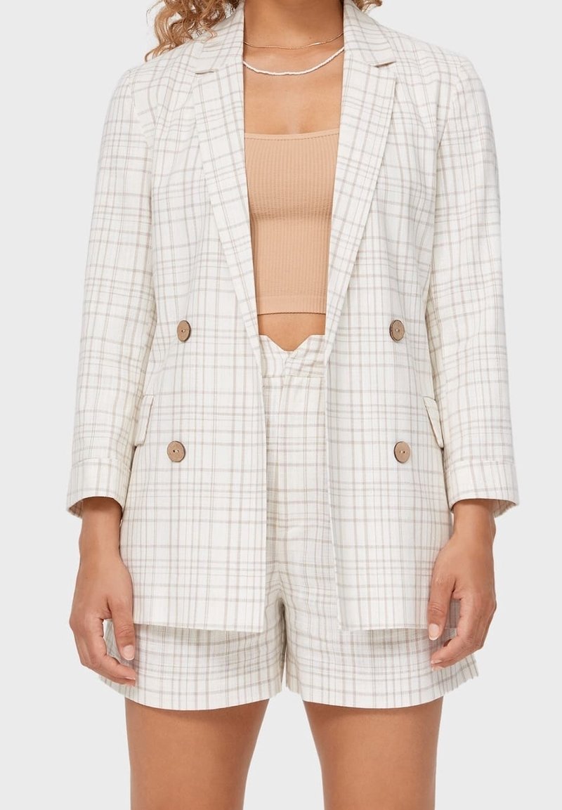 Blazer à carreaux beige clair et crème, présentant un design croisé avec des boutons en bois, accompagné d'un short assorti.