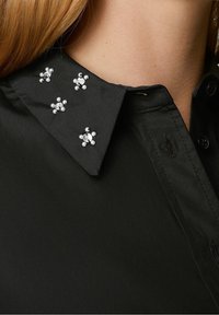Colletto di camicia nero decorato con ornamenti argento e perlacei a motivo floreale, con una texture del tessuto liscia.