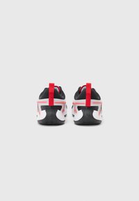 Black and white athletic shoes with red accents, featuring a cushioned sole, pull tab, and textured outsole for grip.