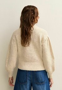 Roomkleurige gebreide sweater met een geribbeld zoom en pofmouwen, gecombineerd met donkerblauwe denim shorts. Gestructureerde stof met een zachte uitstraling.