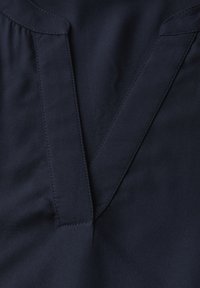 Navyblauer Stoff mit einem V-Ausschnitt und strukturierten Falten. Glatte Textur mit kontrastierenden Nähdetails entlang der Kanten.