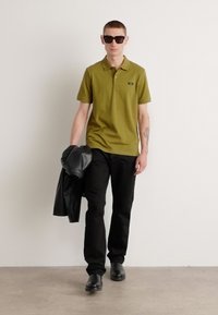 Camiseta polo verde oliva con cuello, jeans negros y chaqueta de cuero negra, complementada con gafas de sol oscuras y zapatos negros.