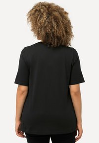 Camiseta negra de manga corta con un ajuste relajado. Fabricada en algodón suave, cuenta con un cuello redondeado y una textura lisa.