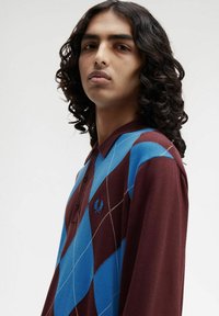 Polo di colore bordeaux con motivo argyle blu, cuciture bianche e colletto con bottoni. Logo ricamato sul petto. Tessuto morbido.