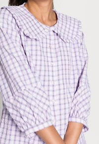 Lilla gingham skjorte med flæset krave, knaplukning foran og pufærmer. Struktureret bomuldsstof tilføjer visuel interesse.