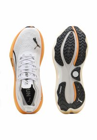 Zapatillas deportivas blancas con parte superior de malla transpirable, suela de acento naranja y suela de tracción de goma negra. Presentan la marca Puma.