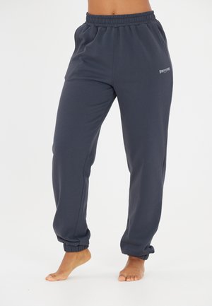 Pantalons de sport bleu marine avec une taille élastique, des chevilles resserrées et un petit logo imprimé sur le côté. Texture douce et lisse.