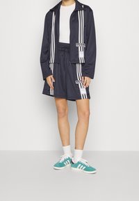 Marintröja och shorts med vita vertikala ränder, med Adidas-loggor. Bärs med turkosa sneakers och vita strumpor.