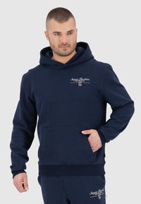 Navigatieblauwe hoodie van zacht materiaal, voorzien van een voorzak, geribde manchetten en witte logo-details op de borst. Klassieke pasvorm.