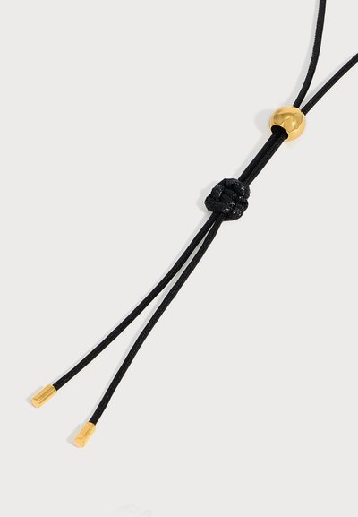 Collier à cordon réglable noir avec une perle dorée et deux extrémités dorées sur un fond clair.