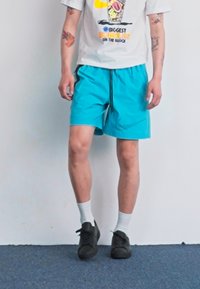 Turquoise swim shorts with a drawstring waist, paired with a white graphic t-shirt, black shoes, and white socks. Casual summer outfit.