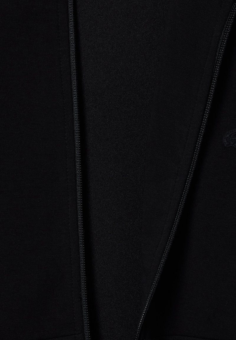 Felpa nera con zip, dotata di tessuto liscio, fodera interna testurizzata e un logo embosso discreto nella zona del petto.