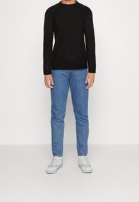 Schwarzer, gestrickter Pullover mit langen Ärmeln und Rundhalsausschnitt, kombiniert mit hellblauen Jeans und weißen Sneakers mit roten Akzenten.